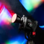 Projecteur Aputure 1000c avec un faisceau lumineux coloré, monté sur un trépied, émettant des lumières rouges, bleues et vertes.