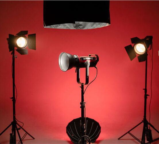 Projecteur monté sur un trépied avec un éclairage de fond rouge, entouré de deux autres projecteurs sur des supports.